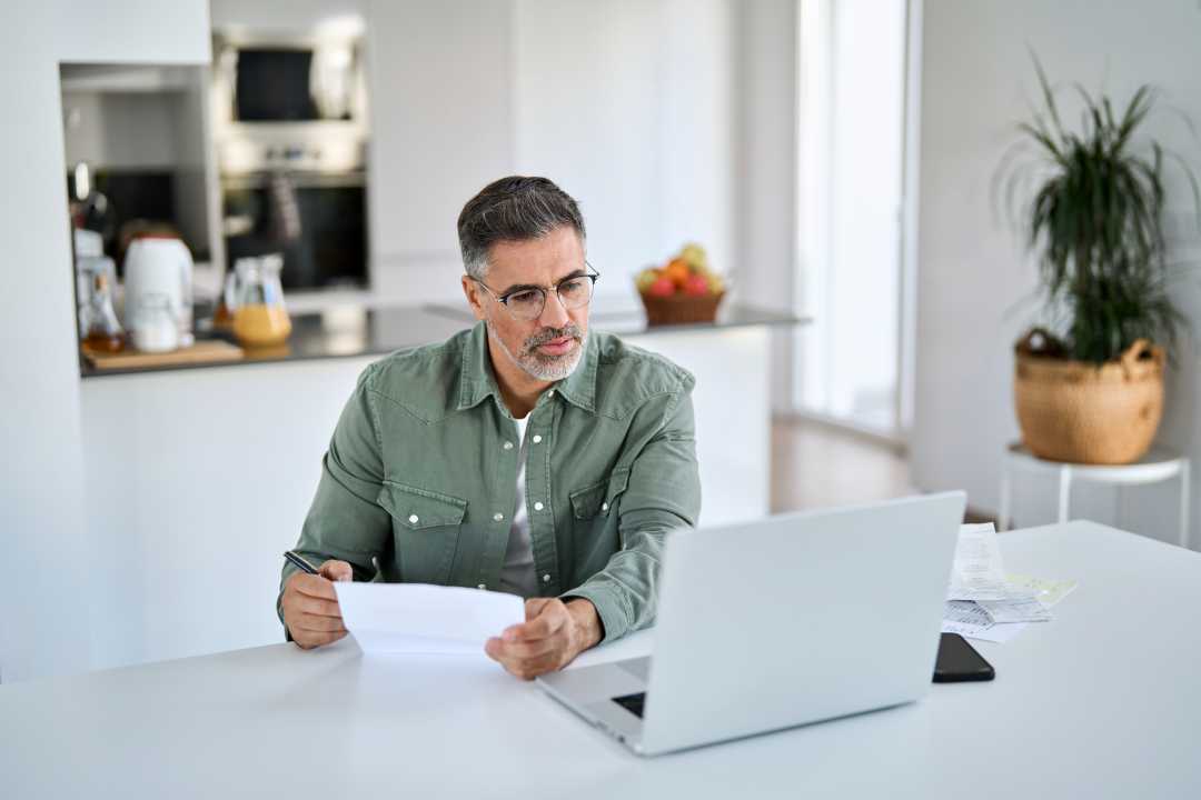 Man with laptop and papers in kitchen