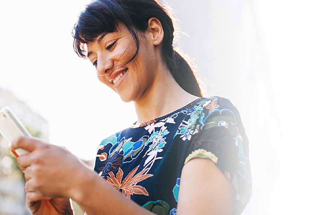 Young smiling woman holding phone with clear sky behind her