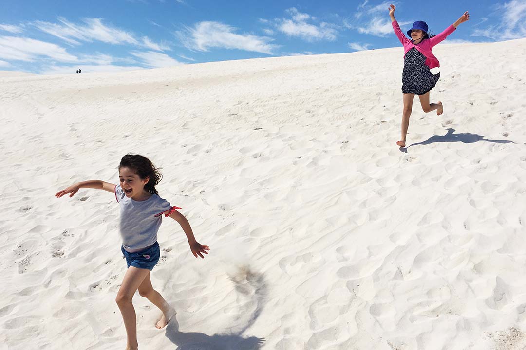 Two kids running down sand dunes